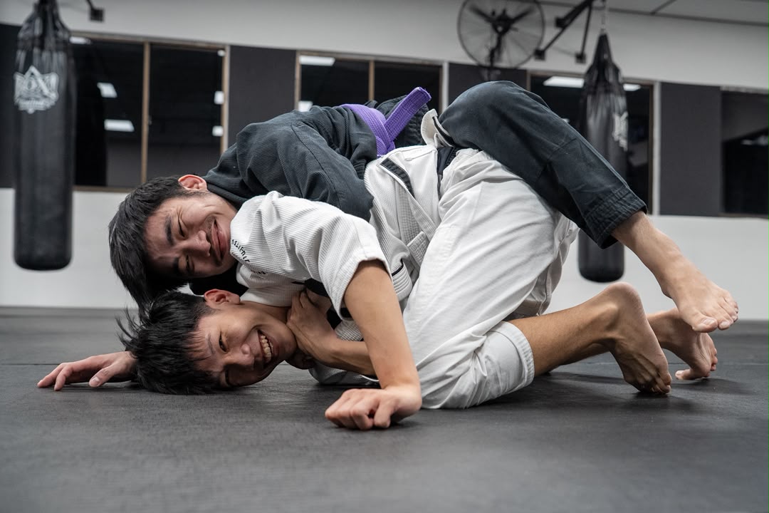 Two BJJ students laughing mid-roll on the mats