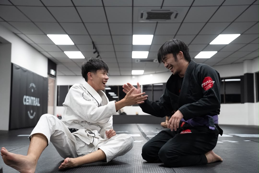 Two BJJ students laughing and high-fiving on the mats after a roll
